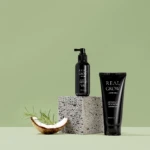 Real Grow hair care products (pump spray and tube) placed on a textured block with a coconut slice and rosemary against a green background.