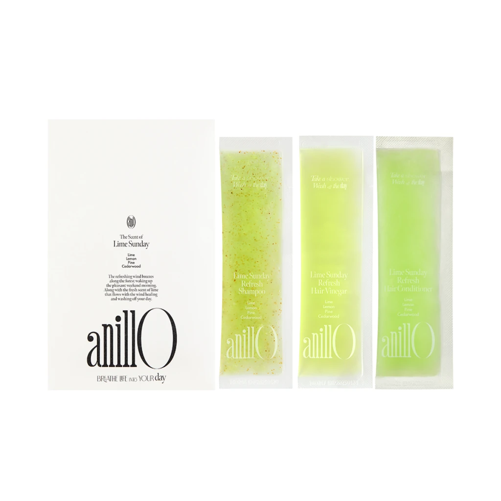 White box with the 'anillO' logo and the slogan 'BREATHE LIFE INTO YOUR day' sits beside four lime-green sachets of Lime Sunday products, from left to right including a speckled sample and three solid lime sachets labeled 'Refresh Shampoo', 'Refresh Hair Vinegar', and 'Refresh Hair Conditioner'.