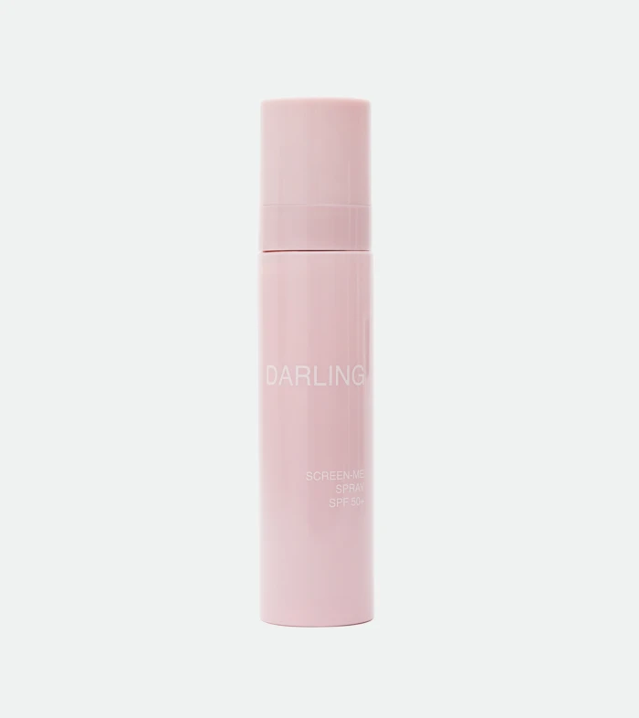 Vertical close-up of a pink cosmetic bottle with text, labeled 'DARLING' and 'SCREEN-ME SPRAY SPF 50+' (tinted skin-tone bottle)
