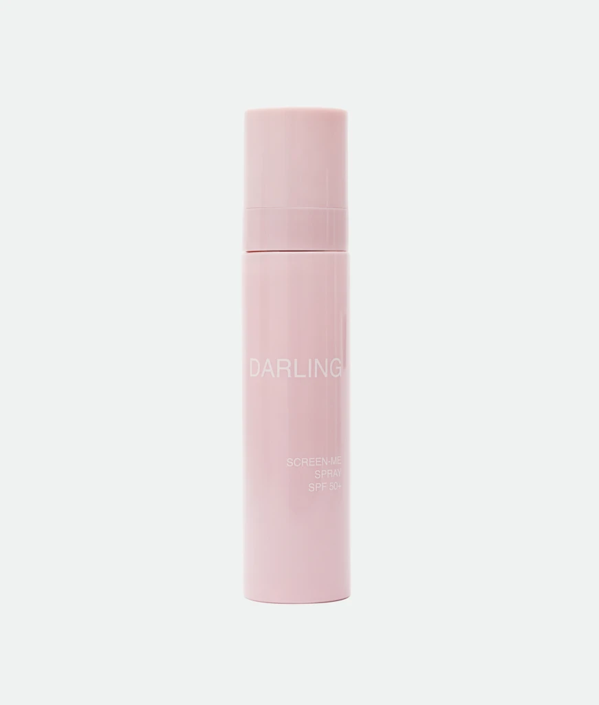 Vertical close-up of a pink cosmetic bottle with text, labeled 'DARLING' and 'SCREEN-ME SPRAY SPF 50+' (tinted skin-tone bottle)