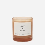 Amber glass candle with a white label reading 'Salt & Stone' and bergamot & hinoki scent notes