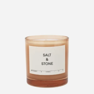 Amber glass candle with a white label reading 'Salt & Stone' and bergamot & hinoki scent notes