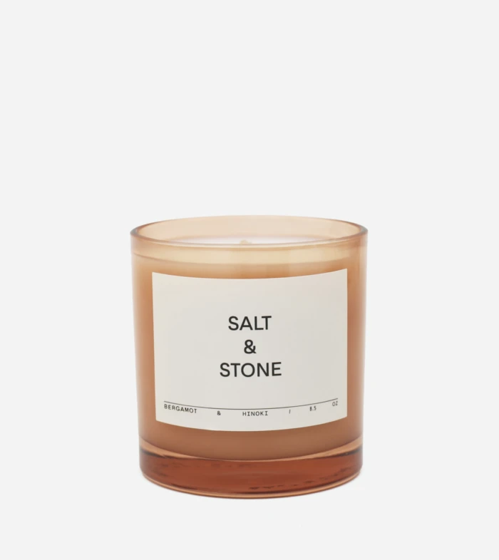 Amber glass candle with a white label reading 'Salt & Stone' and bergamot & hinoki scent notes