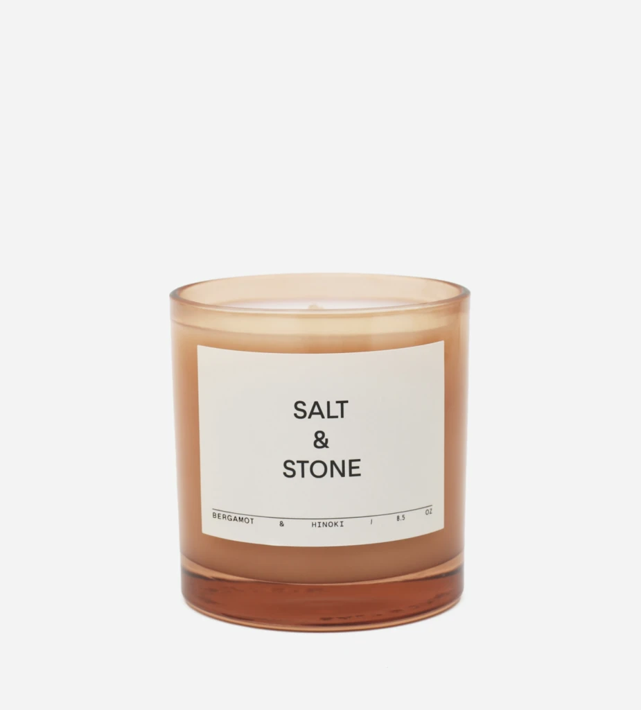 Amber glass candle with a white label reading 'Salt & Stone' and bergamot & hinoki scent notes