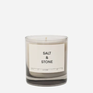 Scented candle in a clear glass jar with a beige label reading 'SALT & STONE' and a single wick visible on top.