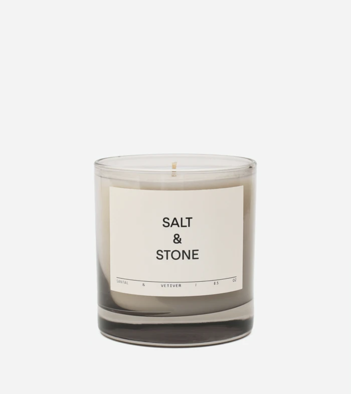 Scented candle in a clear glass jar with a beige label reading 'SALT & STONE' and a single wick visible on top.