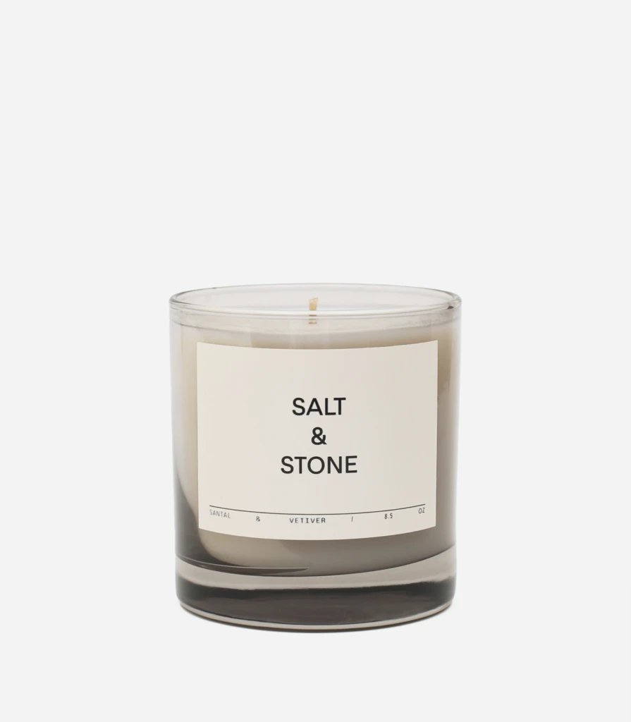 Scented candle in a clear glass jar with a beige label reading 'SALT & STONE' and a single wick visible on top.