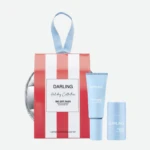 Gift-wrapped red-and-white striped box with a blue ribbon and light-blue Darling skincare tubes, displaying a holiday kit setup