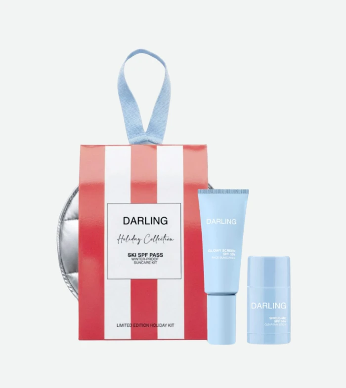 Gift-wrapped red-and-white striped box with a blue ribbon and light-blue Darling skincare tubes, displaying a holiday kit setup