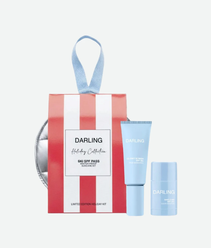 Gift-wrapped red-and-white striped box with a blue ribbon and light-blue Darling skincare tubes, displaying a holiday kit setup