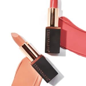Two lipstick bullets with pink and nude shades against a white background, with swatches of lipstick smeared nearby for a makeup product aesthetic.
