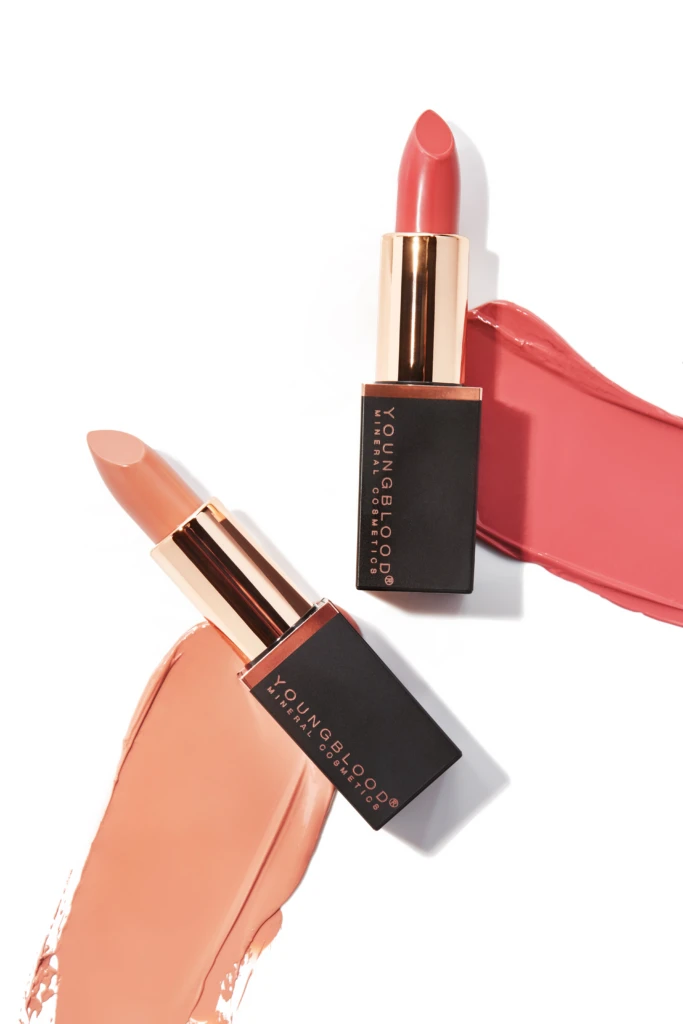 Two lipstick bullets with pink and nude shades against a white background, with swatches of lipstick smeared nearby for a makeup product aesthetic.