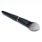 Close-up of a makeup brush with a dark handle and a copper ferrule, fluffy bristles against a white background.
