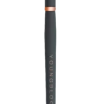 Slim black makeup brush with dense bristles, rose-gold collar, and 'YOUNGBLOOD' printed along the handle.