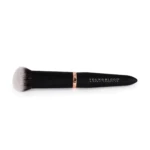 Makeup brush lying on a white background, white bristles and a black handle with a copper band; Youngblood branding visible.