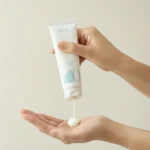 Hands squeeze a white tube, squeezing cream onto an open palm for skincare product demo.