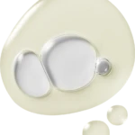 Close-up of a pale cream-colored cosmetic lid with embedded circular wells and a small raised button; two small cream droplets nearby.