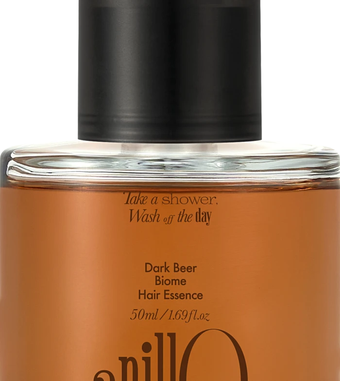 Close-up of a glass bottle with an orange liquid and a black pump, labeled Dark Beer Biome Hair Essence (50 ml).