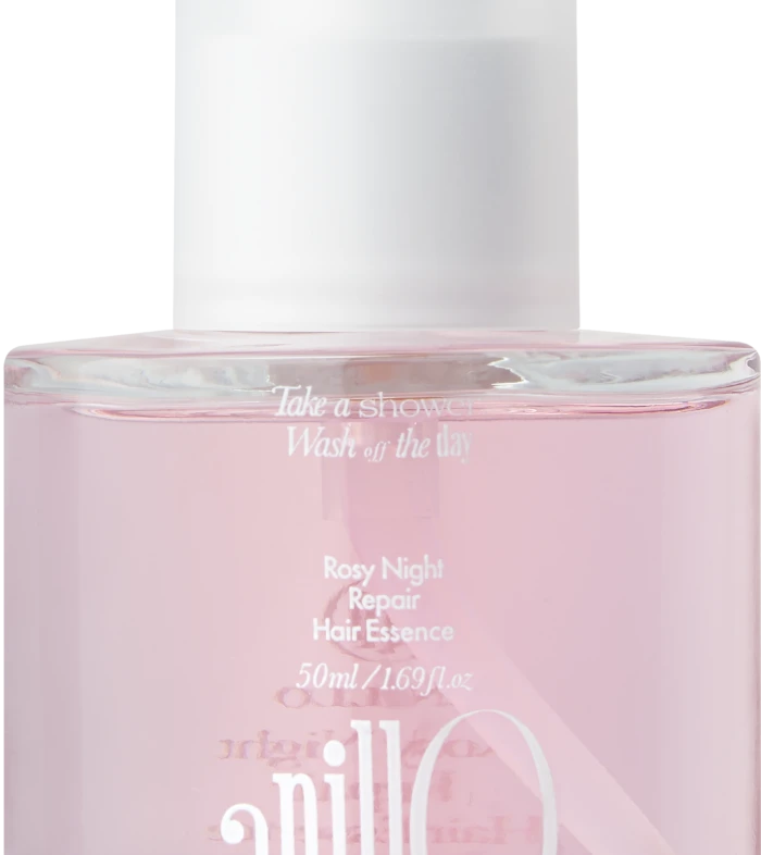 Close-up of a pink cosmetic bottle with a white cap, displaying the label 'Rosy Night Repair Hair Essence'.