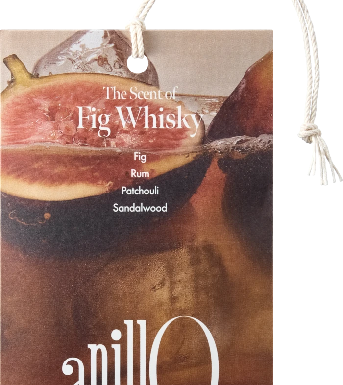 Hanging product tag for a fragrance, reads 'The Scent of Fig Whisky' with notes Fig, Whisky, Patchouli, Sandalwood; rope loop visible.
