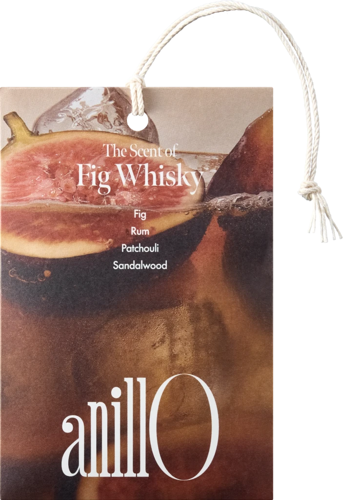 Hanging product tag for a fragrance, reads 'The Scent of Fig Whisky' with notes Fig, Whisky, Patchouli, Sandalwood; rope loop visible.