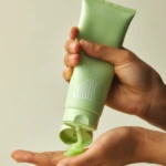 Hands hold a mint-green tube and squeeze out a small amount of product onto the palm, a hair conditioner tube in use.