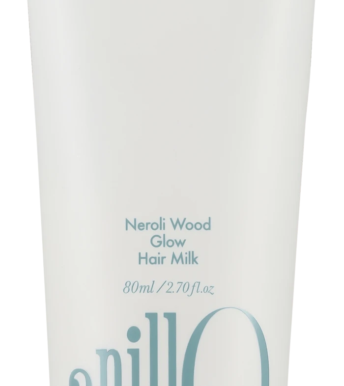 White hair milk tube labeled Neroli Wood Glow Hair Milk with blue slogan 'Take a shower, Wash off the day' and a large blue 'anillo' logo on the side.