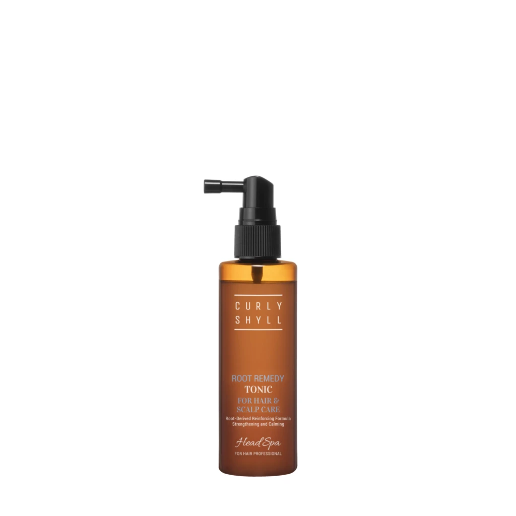 Orange bottle with black pump dispenser, showing product label reading 'CURLY SHYLL' and 'ROOT REMEDY TONIC FOR HAIR & SCALP CARE' for hair treatment.