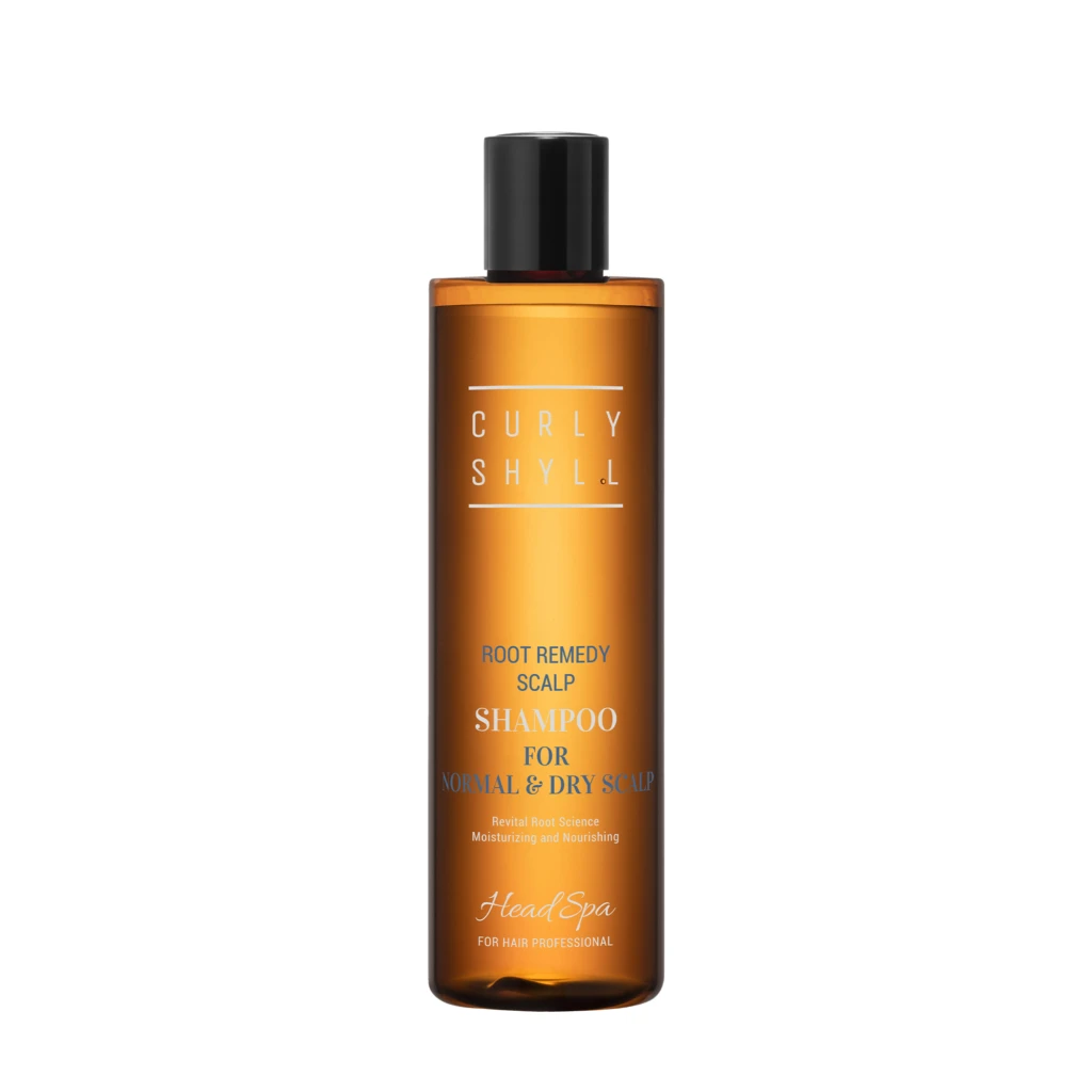 Orange shampoo bottle with a black cap, label reads 'Root Remedy Scalp Shampoo' for normal and dry scalp against a white background in a close-up shot.