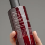 Close-up of a red shampoo bottle labeled 'After Salon Care Shampoo' being held between fingers.