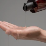 A hand pours liquid from a brown bottle onto the other palm.