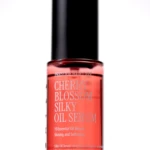 Red glass serum bottle with a tall black cap, labeled Cherry Blossom Silk Oil Serum (Prestige Hair Care).