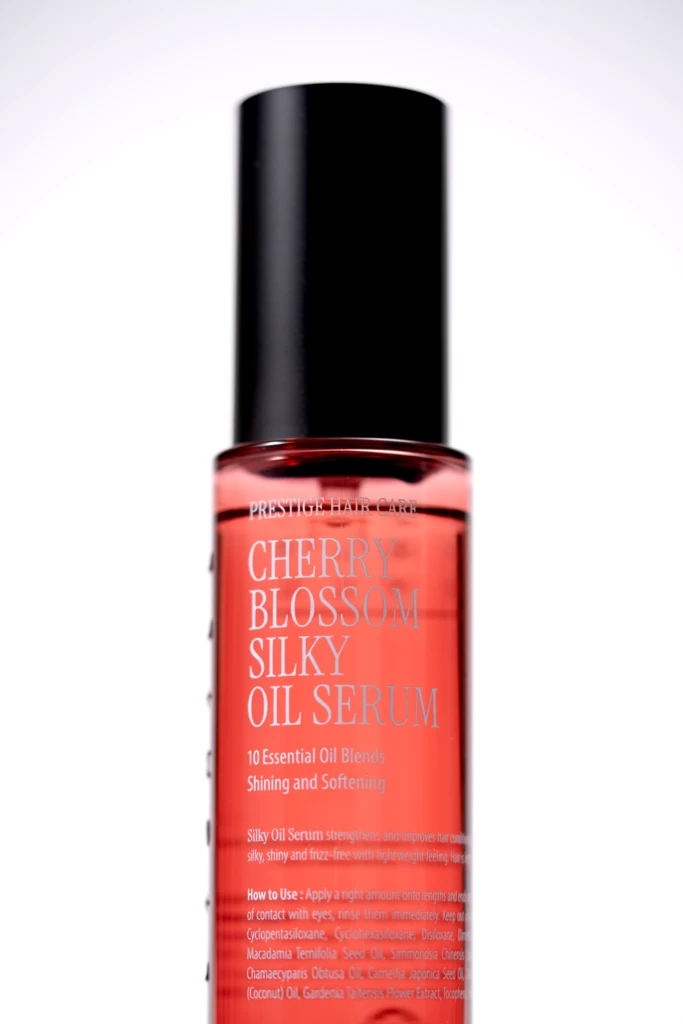 Red glass serum bottle with a tall black cap, labeled Cherry Blossom Silk Oil Serum (Prestige Hair Care).