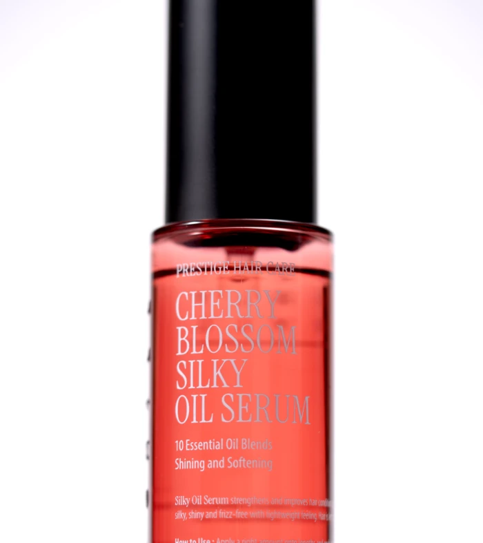 Red glass serum bottle with a tall black cap, labeled Cherry Blossom Silk Oil Serum (Prestige Hair Care).