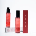 Two red Cherry Blossom Silky Oil Serum bottles with black pump tops stand on a white surface beside a tall red box against a white background.