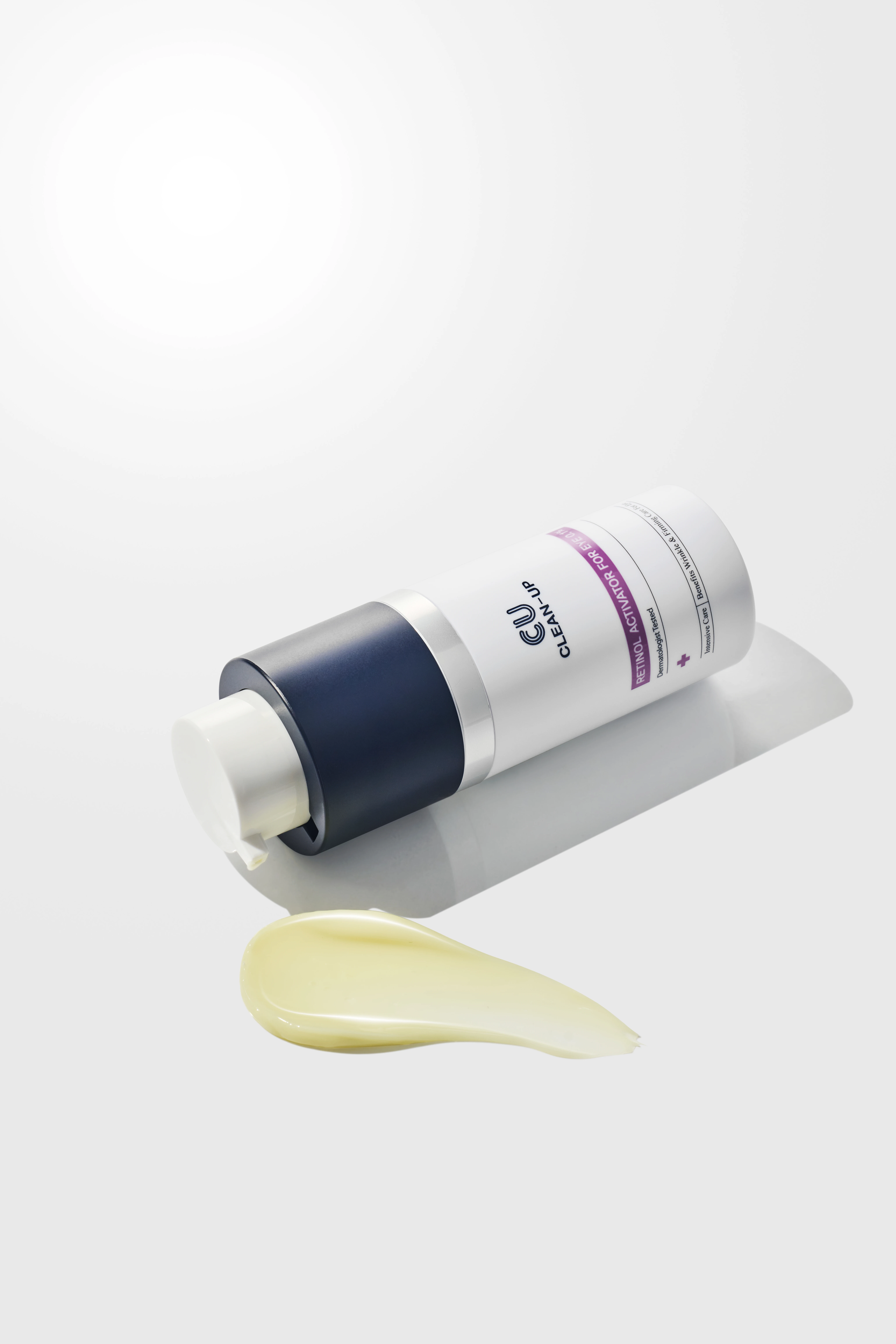 White skincare tube with a dark blue cap lying diagonally on a light surface, with a pale yellow cream swatch in front.