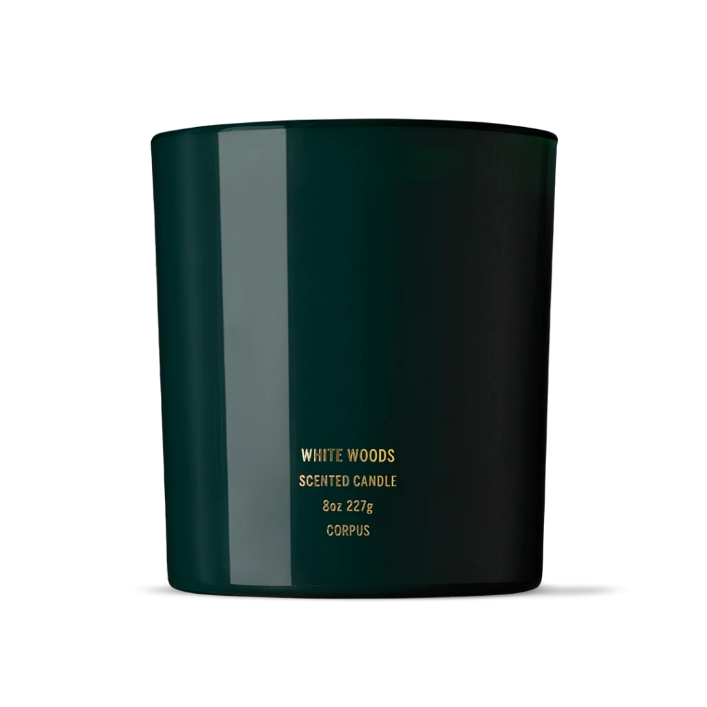 Dark green scented candle in a cylindrical jar with gold text reading 'WHITE WOODS' on the front (8oz).