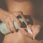 Close-up of a caregiver applying lotion to a baby's chest, with droplets of water on the skin.