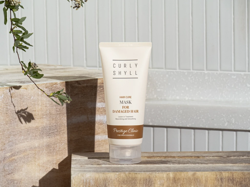 Tube of Curly Shyll Hair Cure Mask for damaged hair resting on a wooden step outdoors.