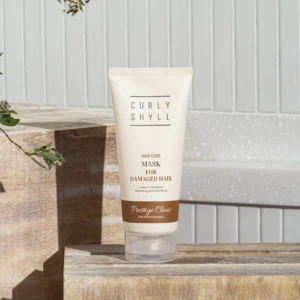 Tube of Curly Shyll Hair Cure Mask for damaged hair resting on a wooden step outdoors.