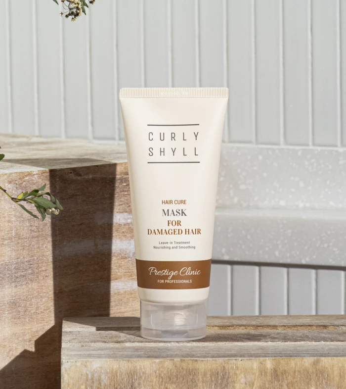 Tube of Curly Shyll Hair Cure Mask for damaged hair resting on a wooden step outdoors.