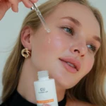 Close-up of a woman applying skincare serum to her cheek with a dropper