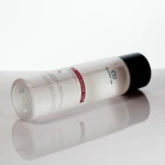 White cosmetic bottle with a black cap lying diagonally on a glossy white surface, labeled as collagen-boosting toner.