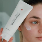 Close-up of a person applying facial cream from a white tube to their cheek.