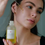 Close-up of a woman applying facial serum to her cheek with a dropper.