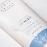 White tube of a scalp-purifying product with a blue design; a blob of lotion sits over the label.